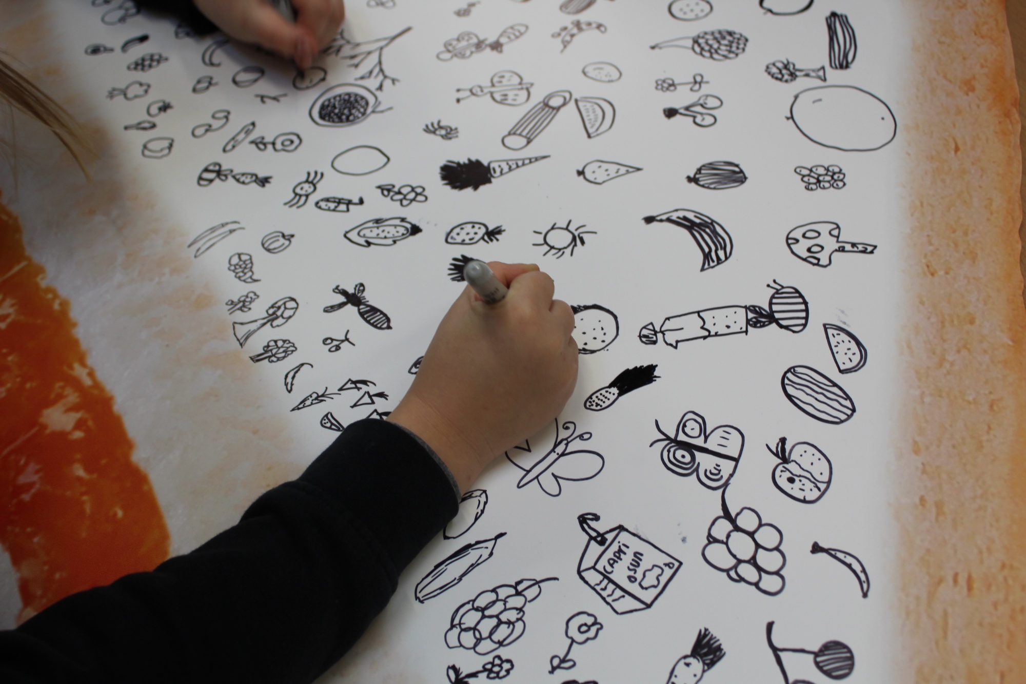 Small hands hold a black Sharpie pen over a page covered in cartoon-like drawings
